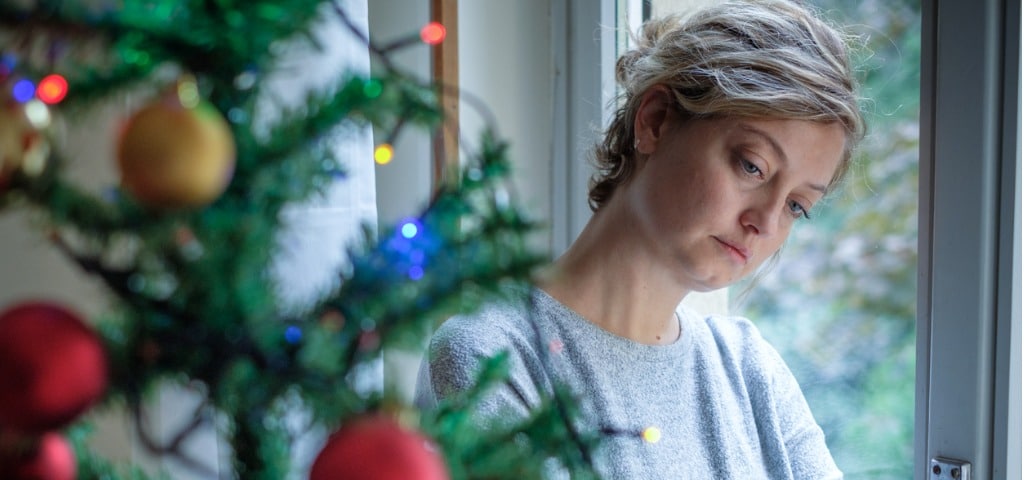 A woman feeling sad and waiting by a Christmas tree