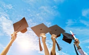 Four hands holding graduation hats on background of blue sky